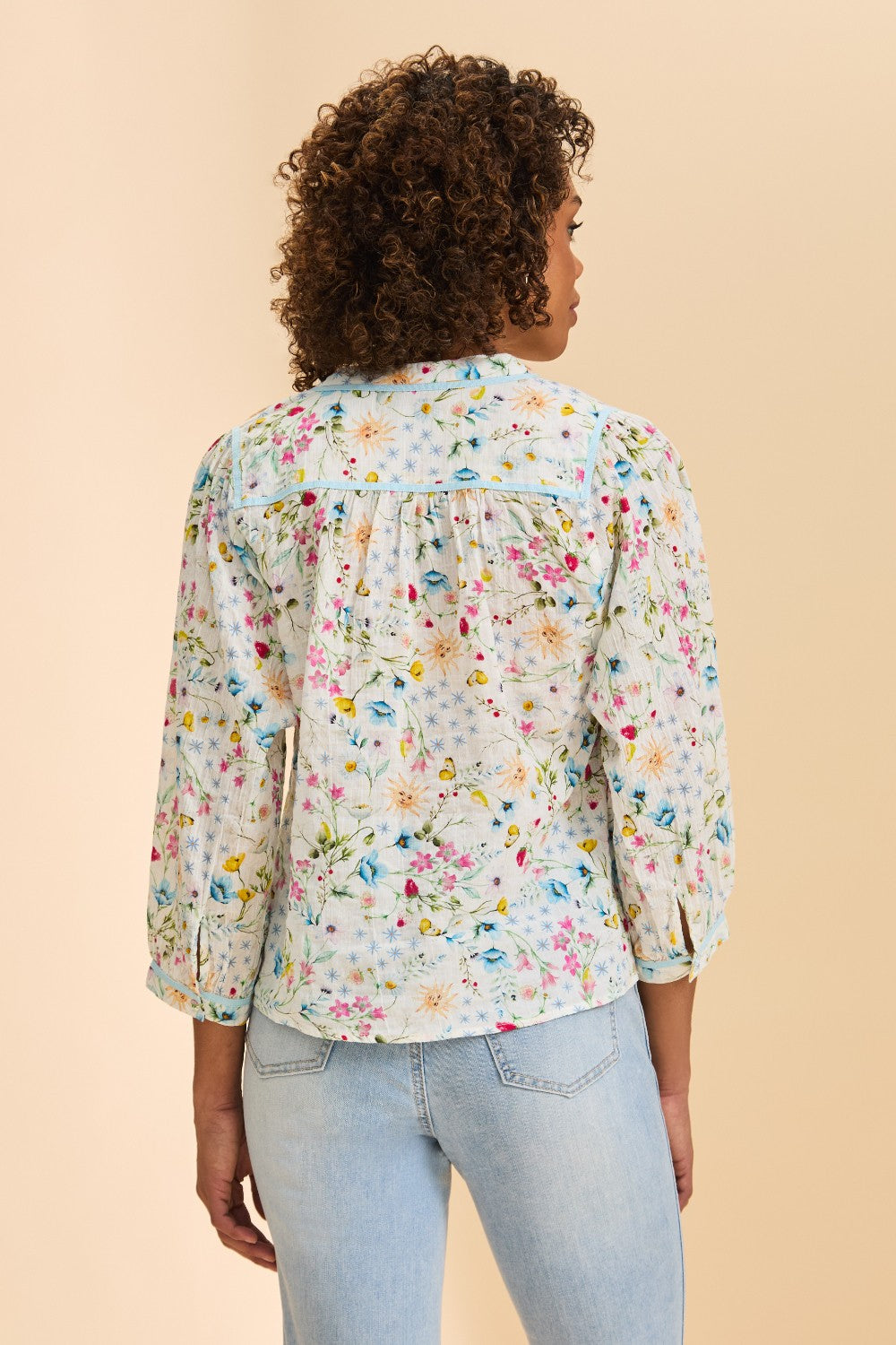Woman wearing a floral blouse and light blue jeans on a beige background