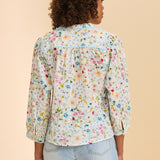 Woman wearing a floral blouse and light blue jeans on a beige background