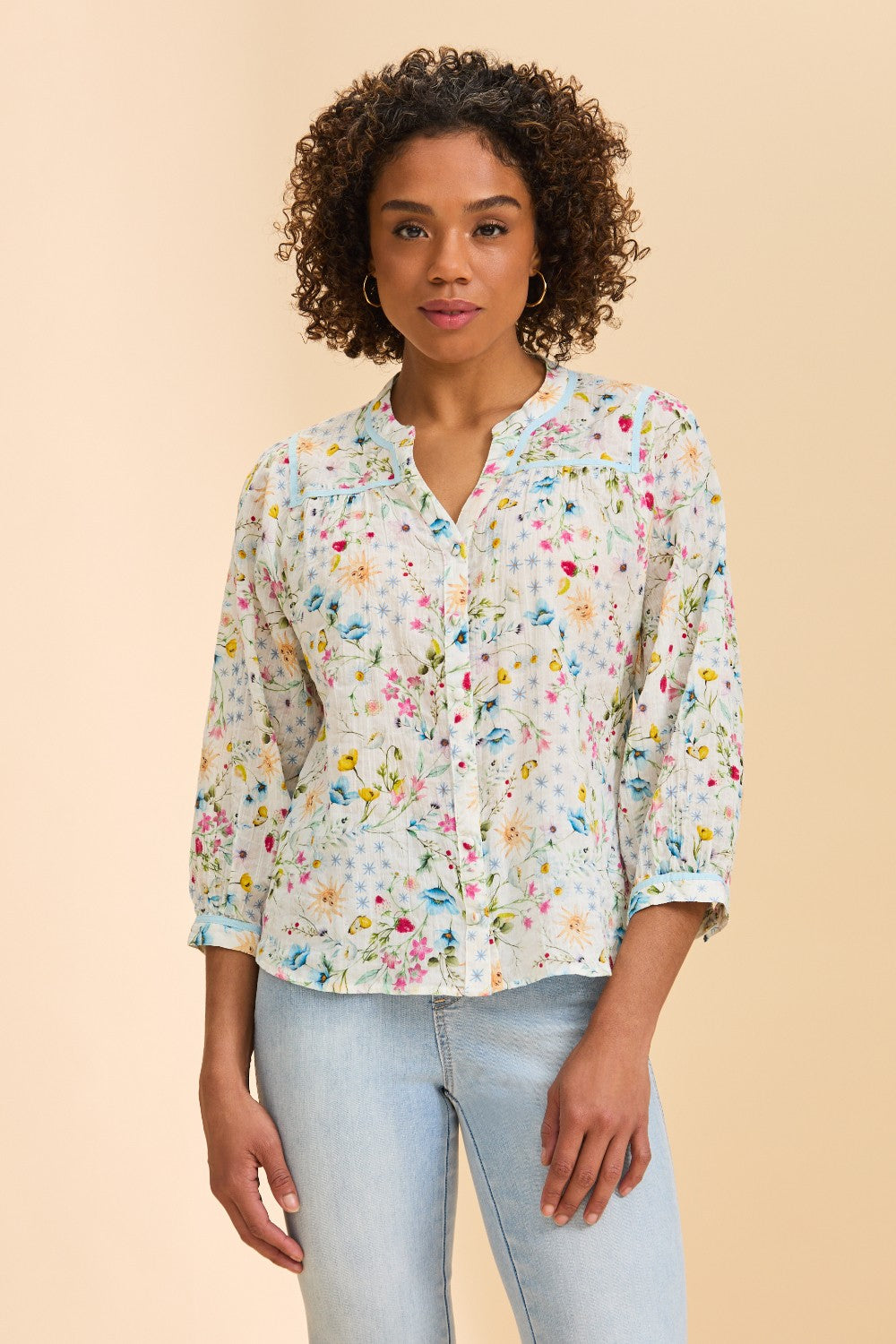Woman wearing a floral blouse and light blue jeans on a beige background
