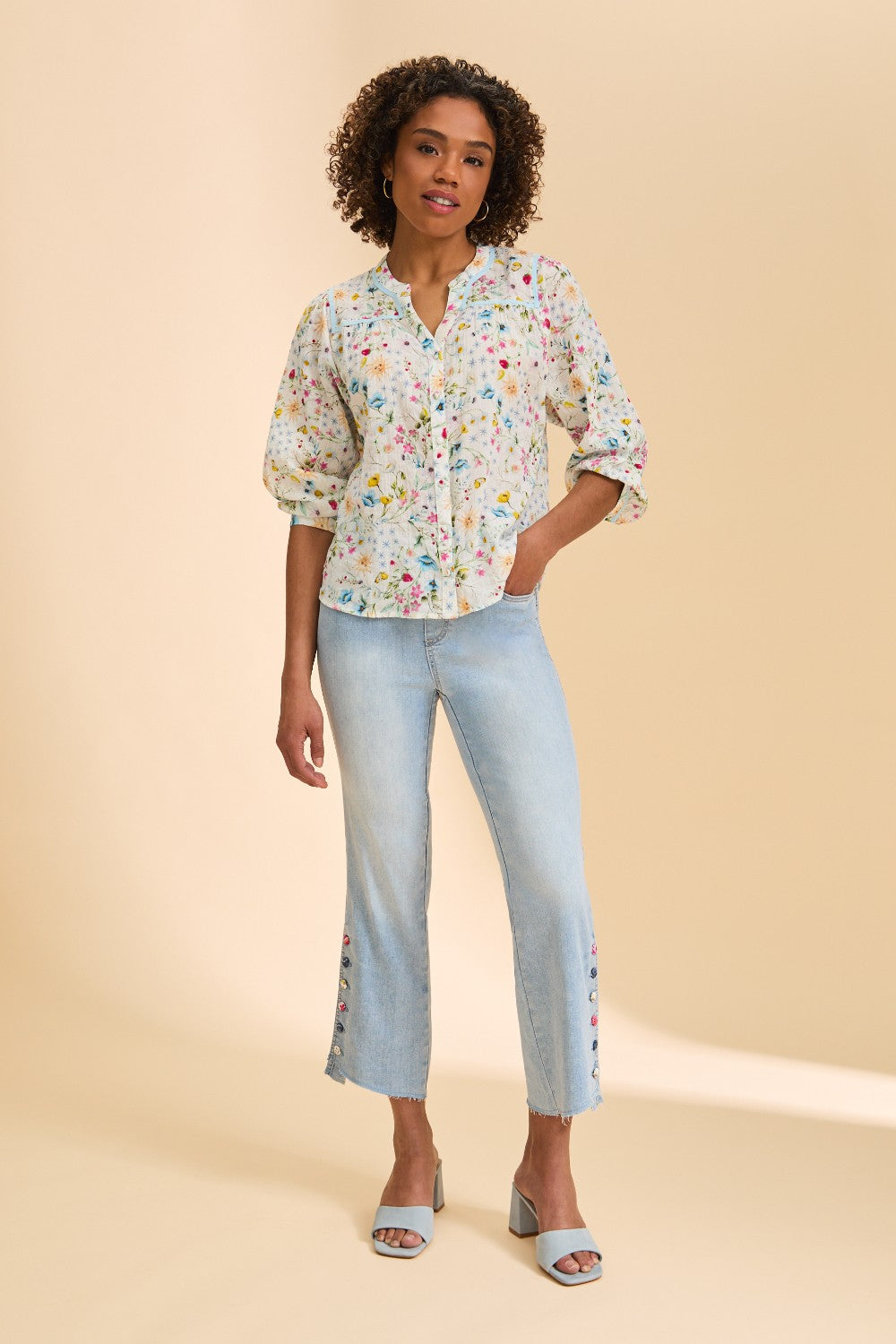 Woman wearing a floral blouse and light blue jeans on a beige background