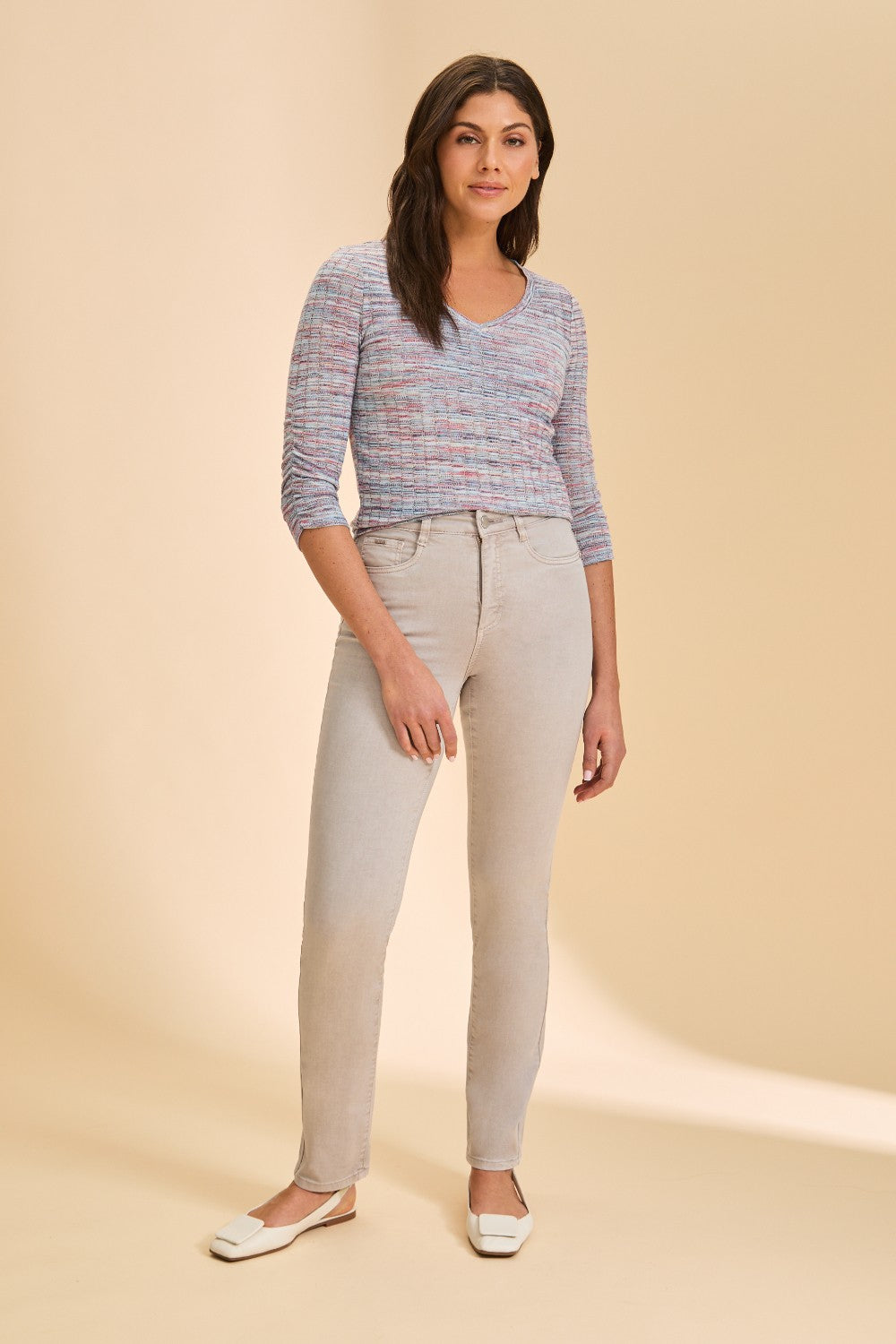 Woman wearing a patterned top and light gray pants on a beige background