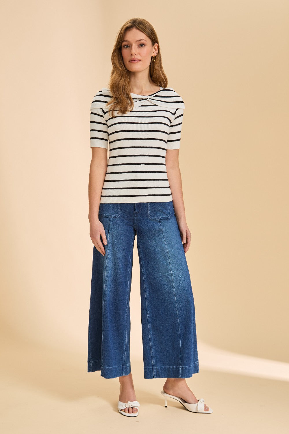 Person wearing black and white striped short sleeve sweater with denim against beige background