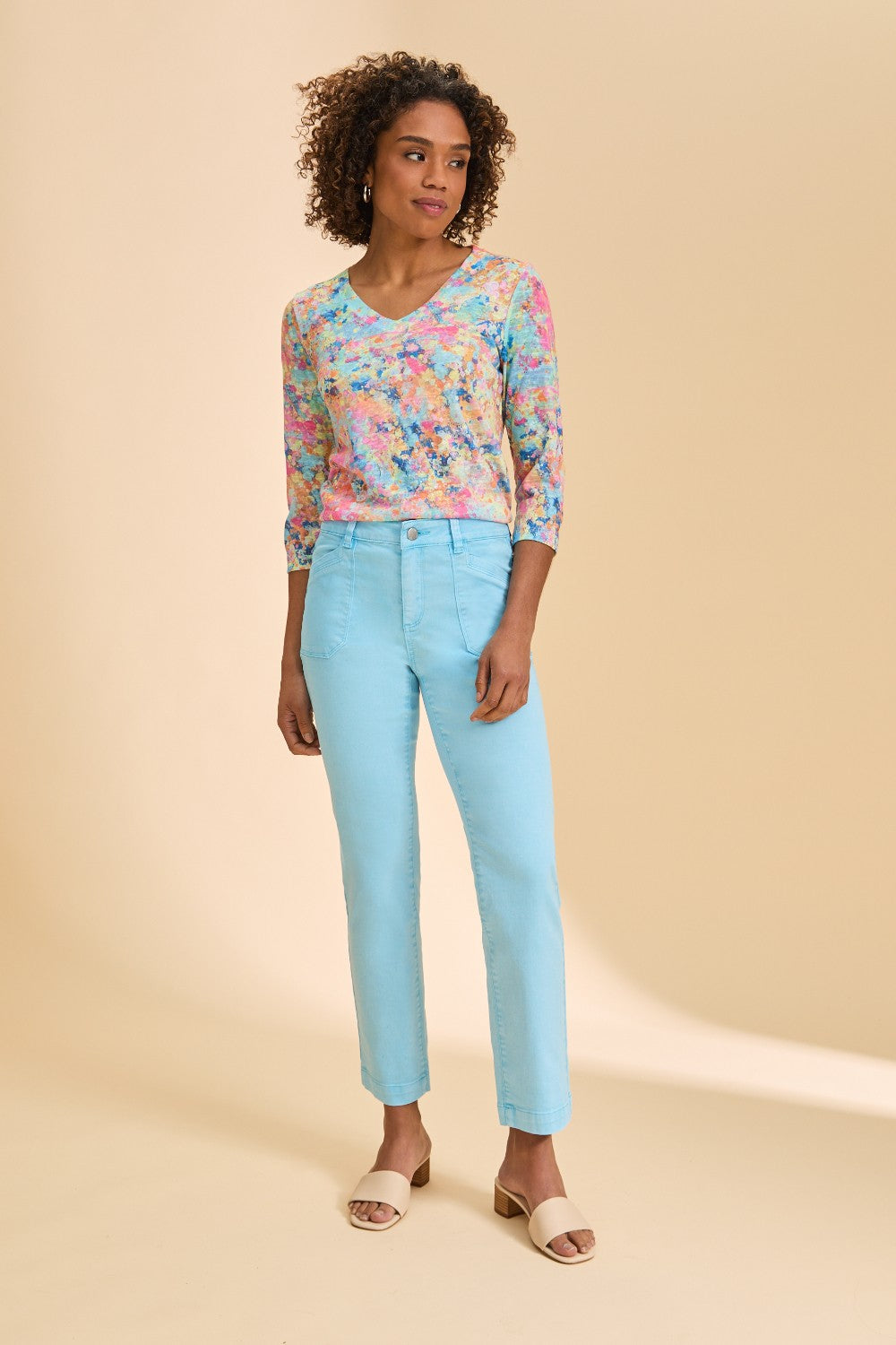 Woman wearing a colorful top and light blue jeans on a beige background