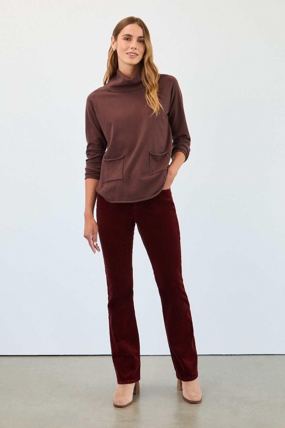 Woman wearing a brown turtleneck and pants against a white background