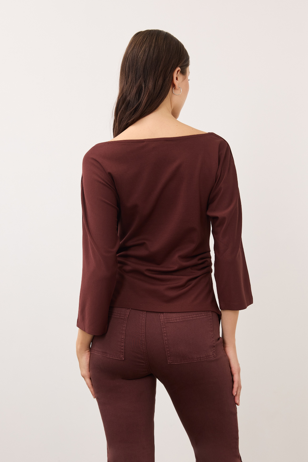 A woman shown from the back wearing a wide-neck, three-quarter sleeve top and matching pants in a deep burgundy color, set against a plain light gray studio background.