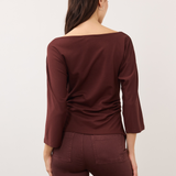 A woman shown from the back wearing a wide-neck, three-quarter sleeve top and matching pants in a deep burgundy color, set against a plain light gray studio background.
