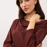 A woman modeling a draped, three-quarter sleeve top in a deep burgundy color against a plain light gray background.
