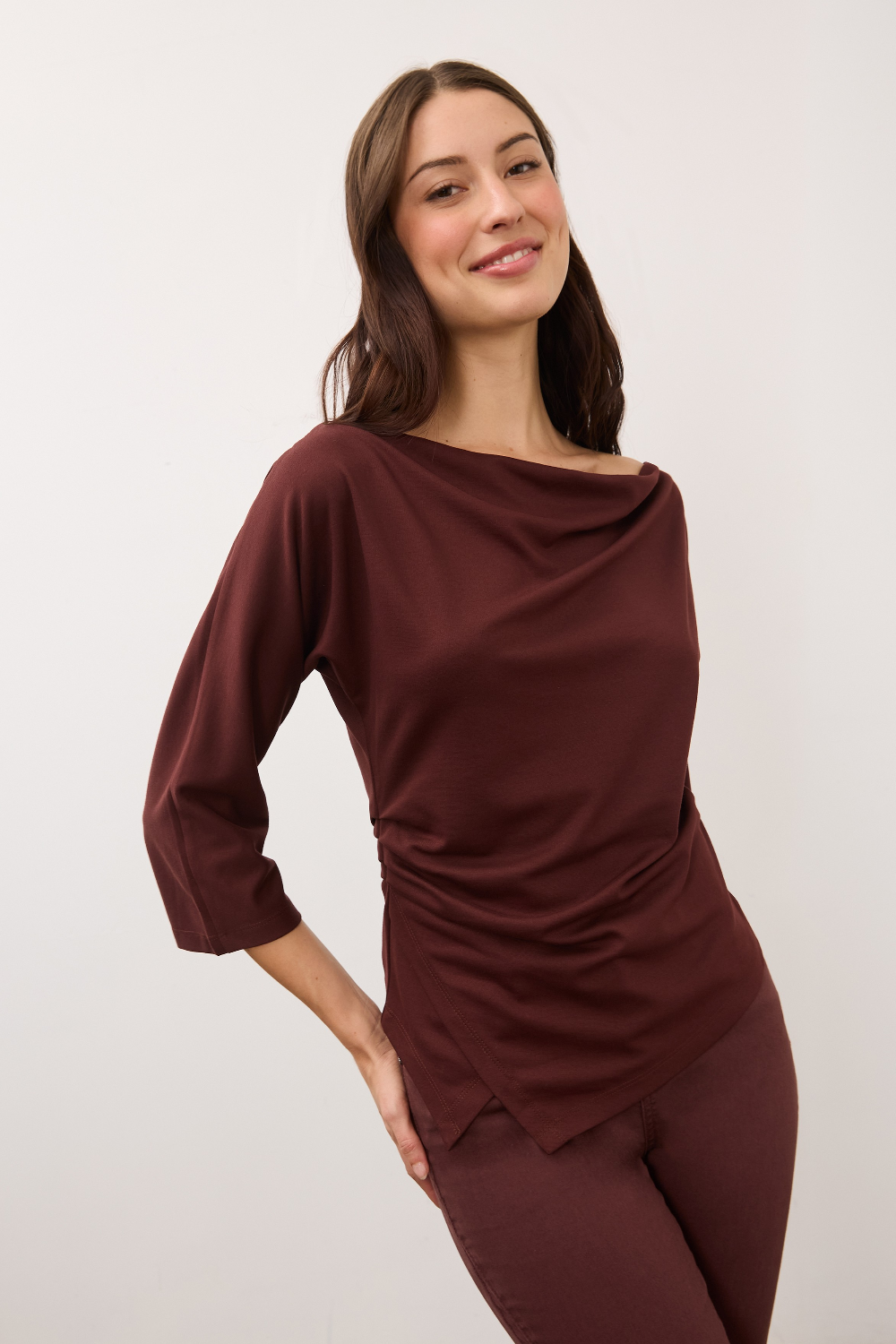 A woman modeling a draped, three-quarter sleeve top in a deep burgundy color, paired with matching pants, against a plain light gray background.