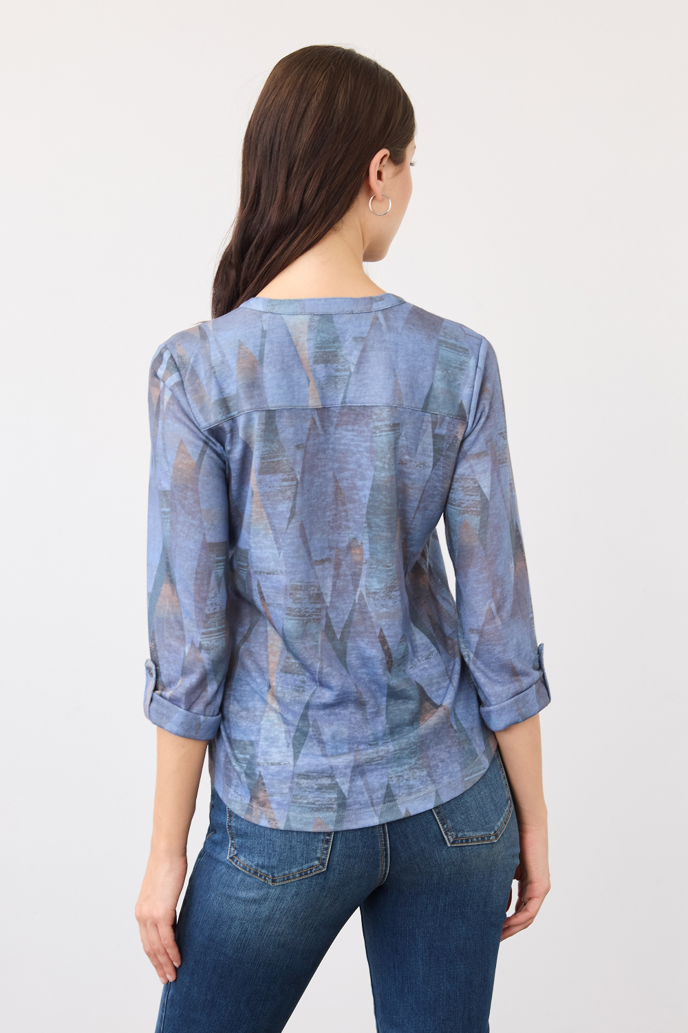 Woman, shown from the back, wearing a blue mixed pattern 3/4 sleeve top with blue jeans on a light background.