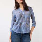 Woman wearing a blue mixed pattern 3/4 sleeve henley top with blue jeans on a light background.