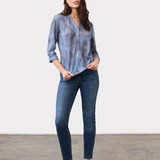 Woman wearing a blue mixed pattern 3/4 sleeve henley top with blue jeans and tan loafers on a light background.