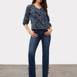 Woman wearing a blue and black floral lace 3/4 sleeve v-neck top with blue jeans and black high heels on a light background.