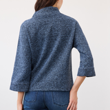 Woman shown from the back wearing a blue 3/4 sleeve mock neck top with blue jeans on a neutral backdrop.