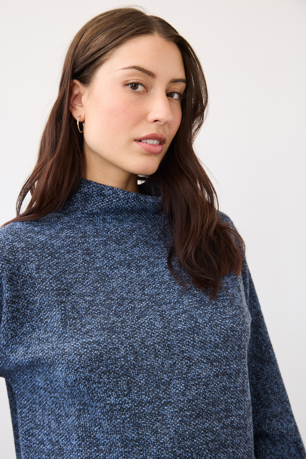 Woman wearing a blue mock neck top on a neutral backdrop.