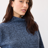 Woman wearing a blue mock neck top on a neutral backdrop.