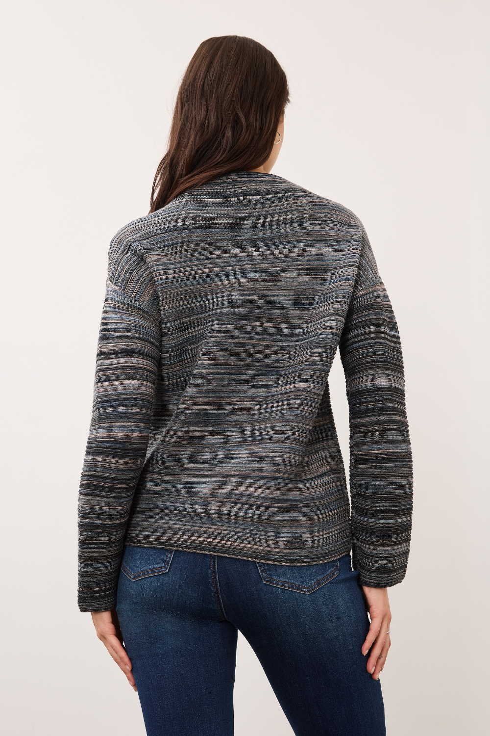 Woman, shown from the back, wearing a blue striped sweater with blue jeans on a light background.