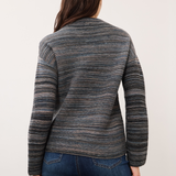 Woman, shown from the back, wearing a blue striped sweater with blue jeans on a light background.