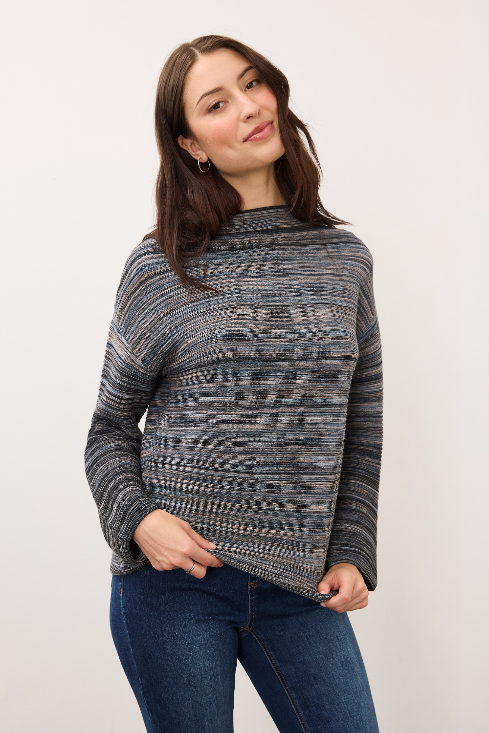 Woman wearing a blue striped sweater with blue jeans on a light background.