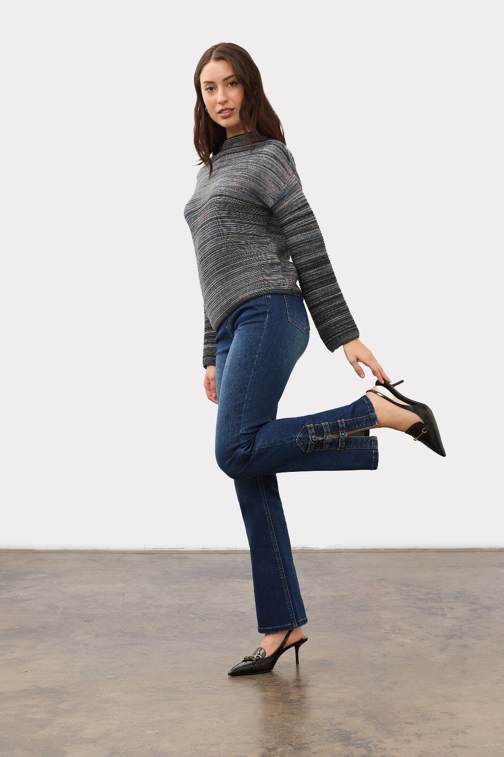 Woman wearing a blue striped sweater with blue jeans and black high heels on a light background.