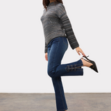 Woman wearing a blue striped sweater with blue jeans and black high heels on a light background.