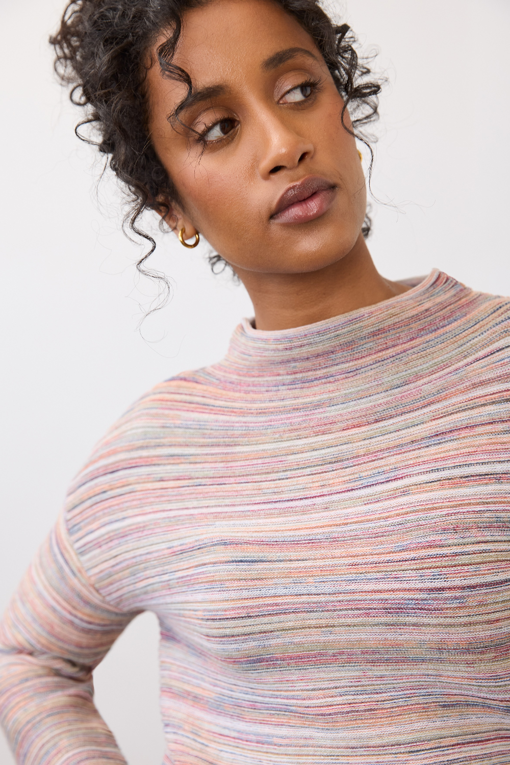 Close up of a woman wearing a multi coloured striped sweater on a light background.