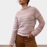 Woman wearing a multi coloured striped sweater with brown cords on a light background.