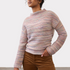 Woman wearing a multi coloured striped sweater with brown cords on a light background.