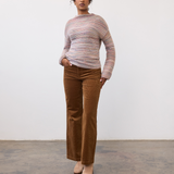 Woman wearing a multi coloured striped sweater with brown cords and tan boots on a light background.