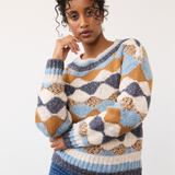 Woman modelling a multi coloured sweater with a houndstooth printed denim photographed against a light background.