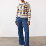 Woman modelling a multi coloured sweater with a houndstooth printed denim and tan boots photographed against a light background.