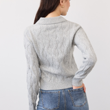 Woman, shown from the back, wearing a gray cable knit sweater, paired with blue jeans, photographed in front of a light studio backdrop.