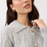 Close up of a woman wearing a gray cable knit cardigan, with a collar and fancy buttons, photographed in front of a light studio backdrop.