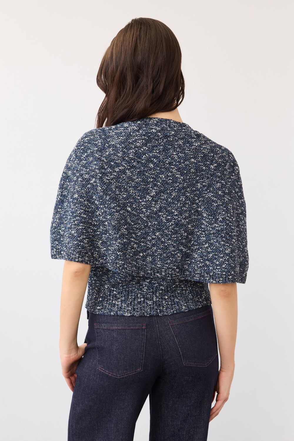 A woman shown from the back wearing a short-sleeve textured knit top in a navy and white speckled pattern, paired with dark denim jeans, against a plain light background.