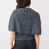 A woman shown from the back wearing a short-sleeve textured knit top in a navy and white speckled pattern, paired with dark denim jeans, against a plain light background.