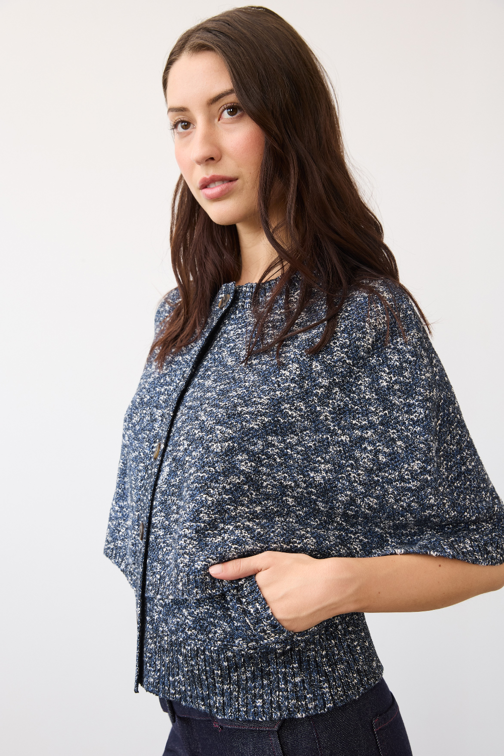 A woman wearing a navy blue and white speckled knit poncho-style cardigan with front pockets, shown from the waist up against a plain light background.