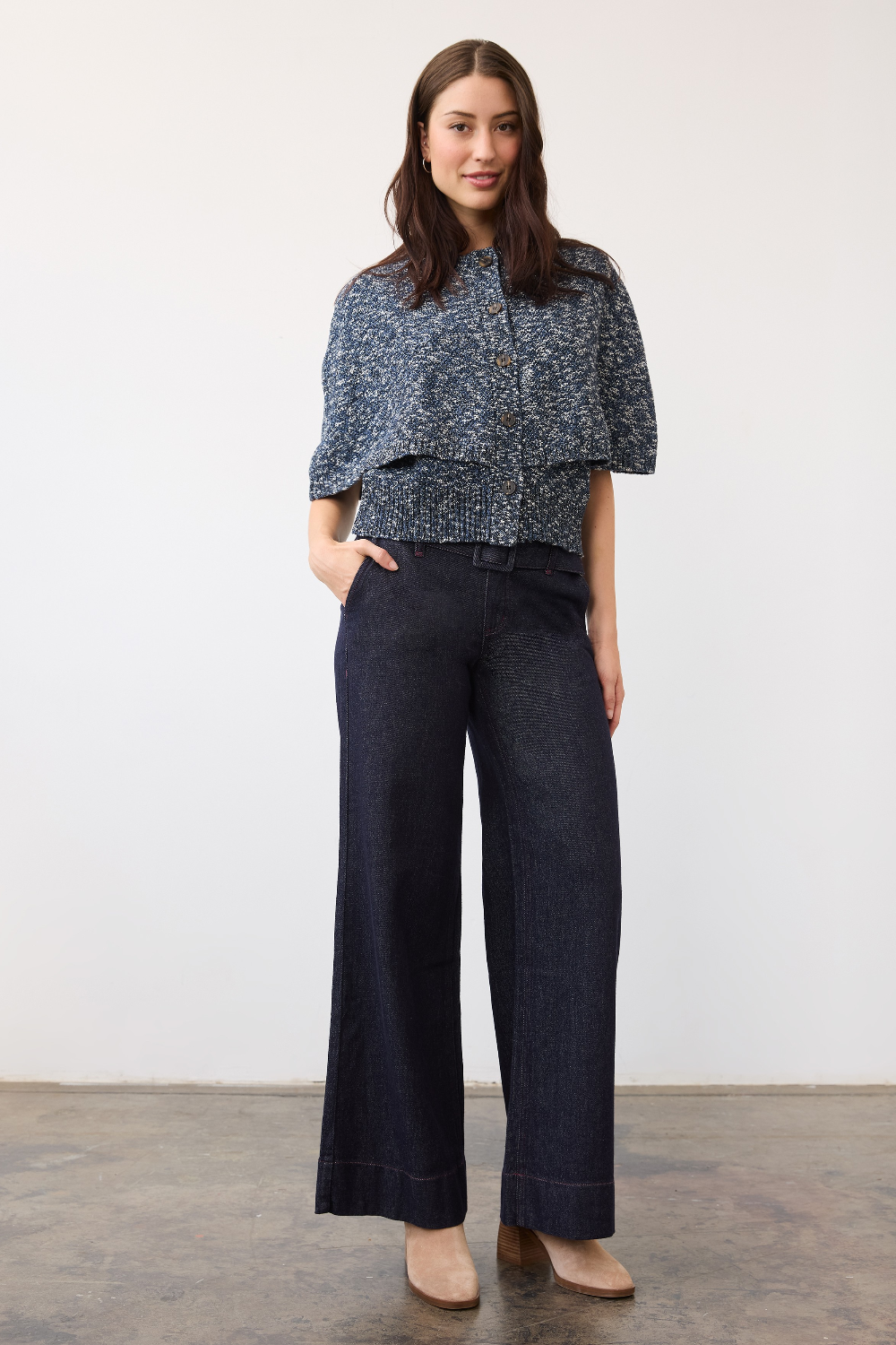 A woman modeling a dark blue patterned short-sleeve sweater with dark wide-leg denim pants and beige heels, standing against a plain white wall.
