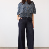 A woman modeling a dark blue patterned short-sleeve sweater with dark wide-leg denim pants and beige heels, standing against a plain white wall.