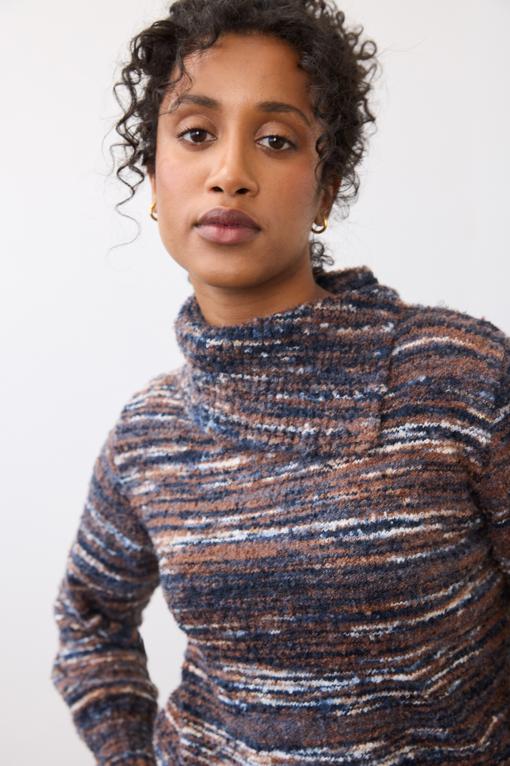 Woman wearing a multi coloured striped sweater on a light background.