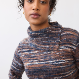 Woman wearing a multi coloured striped sweater on a light background.