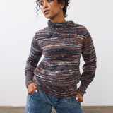 Woman wearing a multi coloured striped sweater with blue cords on a light background.