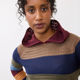 Woman wearing a multi coloured striped knit hoodie against a light backdrop.