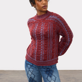 Woman wearing a red and blue mix cable knit crew neck sweater with blue jeans against a light studio backdrop.