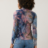 Women, shown from the back, modelling a multi coloured mock neck top with blue jeans photographed against a light background.