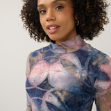 Close up of a women modelling a multi coloured mock neck top photographed against a light background.