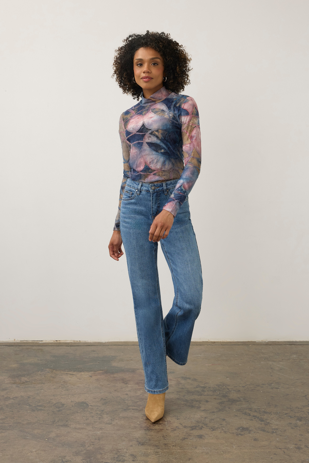 Women modelling a multi coloured mock neck top with blue jeans and tan boots photographed against a light background.