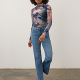 Women modelling a multi coloured mock neck top with blue jeans and tan boots photographed against a light background.