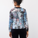 Woman, shown from the back, wearing a patterned top with dark pants on a neutral background.