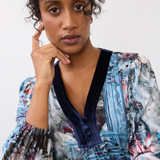 Woman wearing a patterned top, with velvet looking trim on the v-neck, on a neutral background.