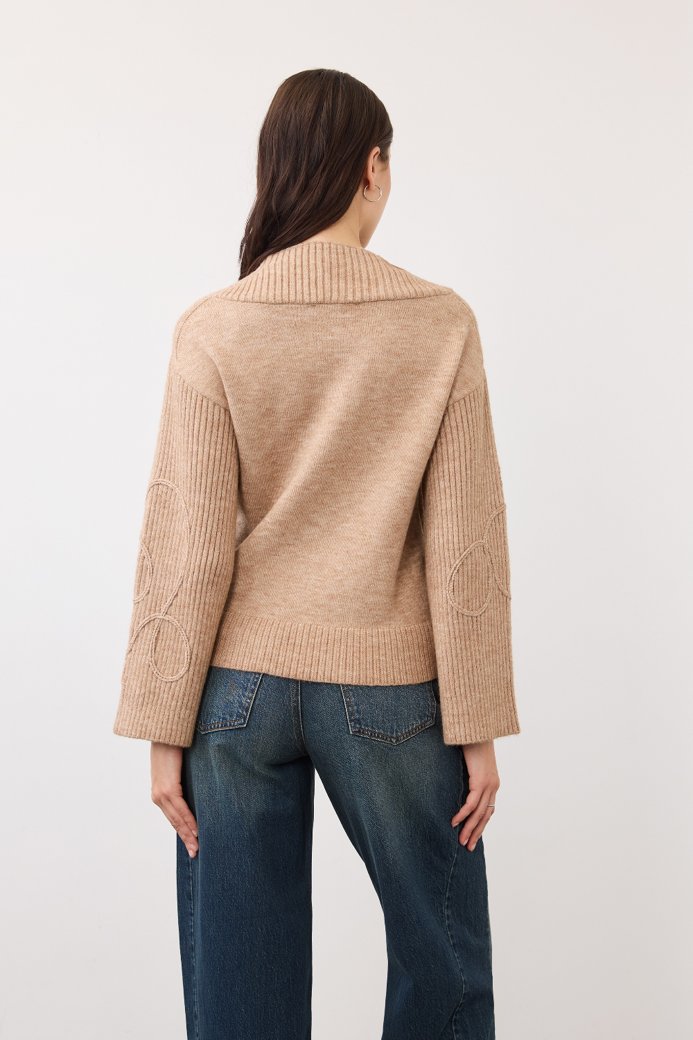 Woman, shown from behind, modelling an embellished tan coloured sweater photographed against a light background.