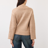 Woman, shown from behind, modelling an embellished tan coloured sweater photographed against a light background.